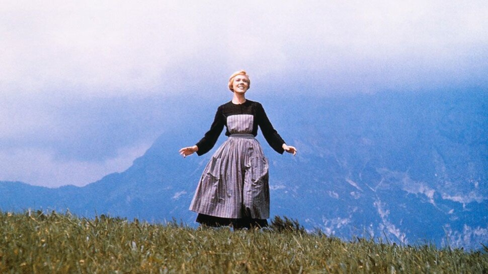 Julie Andrews in Sound of Music, standing on a grassy hill with her arms spread, a look of ecstasy on her face, snowy mountains looming into mist behind her.