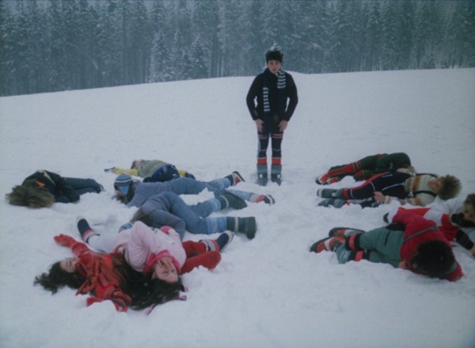 Shot from the film Wolf's Hole, showing a group of teenagers in winter clothes lying on a snowy hillside as if dead, only one of them still standing amidst the pile.