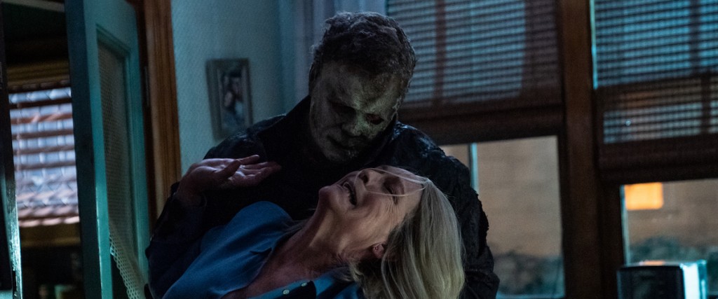 Still from the film Halloween Kills, showing Jamie Lee Curtis grappling with the masked Michael Myers in an office.
