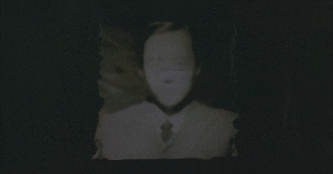 Gif of a shot from the film Cure (1997), showing a picture flapping in a breeze against jet black darkness. The picture is a blurry B&W photo portrait of what appears to be a faceless person in a suit and tie.