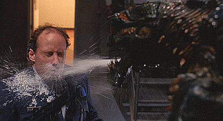 Gif from The Fly II, showing a security guard with a gun being sprayed in the face with a jet of white fluid from the mandibles of a slimy, spiky giant mutant fly-human hybrid hulking in front of him.