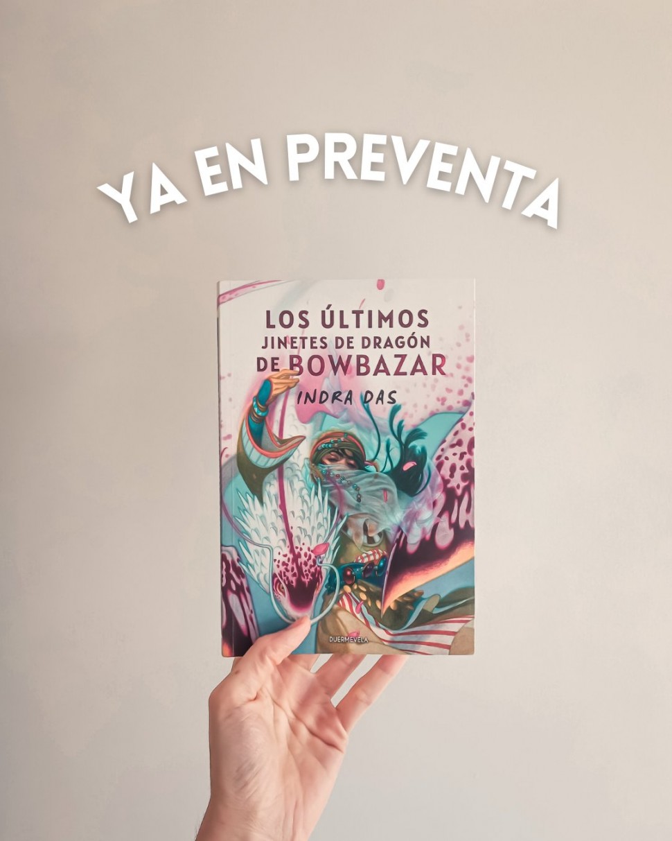 Photo showing a hand holding up the Spanish edition of my novella The Last Dragoners of Bowbazar, Los Ultimos Jinetes de Dragon de Bowbazar, with a colourful painted cover by Tran Nguyen showing a 'dragoner' with a vivid purple, white, orange dragon perched on their shoulder, hand on its neck. Text above the book reads: Ya en preventa